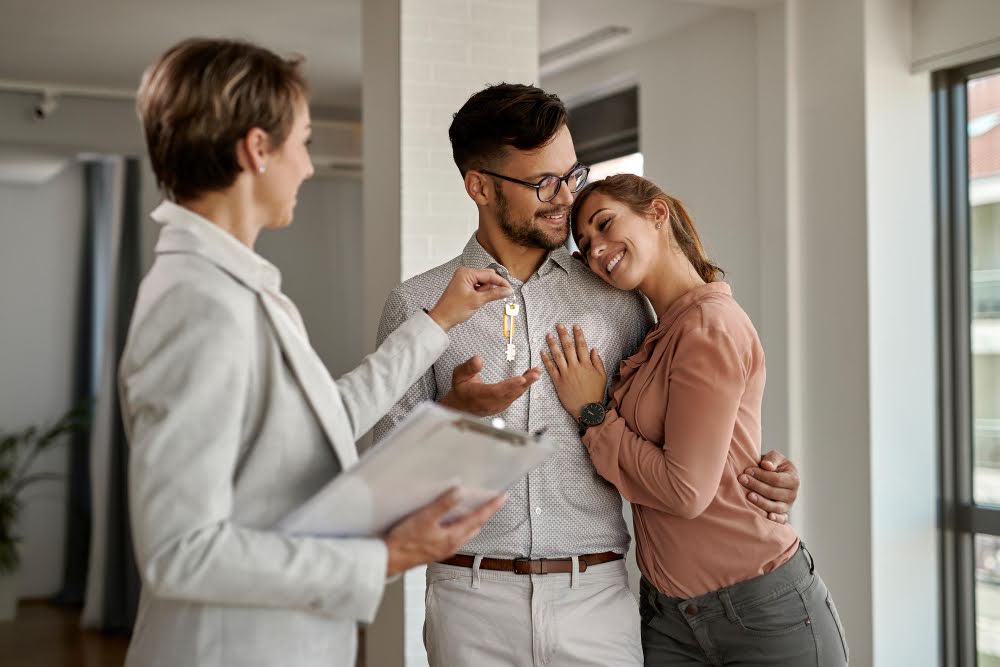 A happy couple buying a home in Utah, smiling as their realtor hands them the keys.