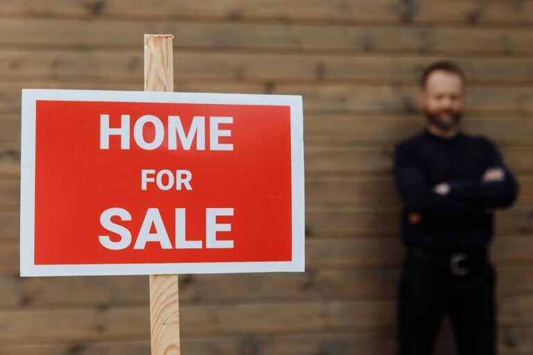 A Utah realtor standing behind a “Home for Sale” sign.