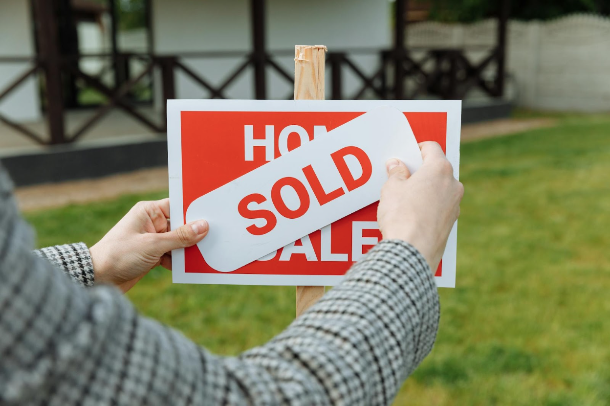A realtor posting a sold sign in front of a house.
