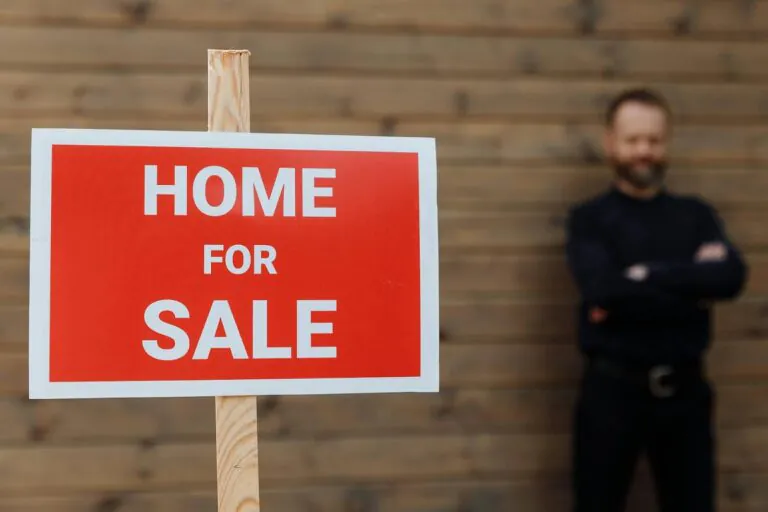 A Utah realtor standing behind a “Home for Sale” sign.